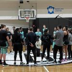 Basketball team huddles on court for discussion.