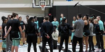 Basketball team huddles on court for discussion.