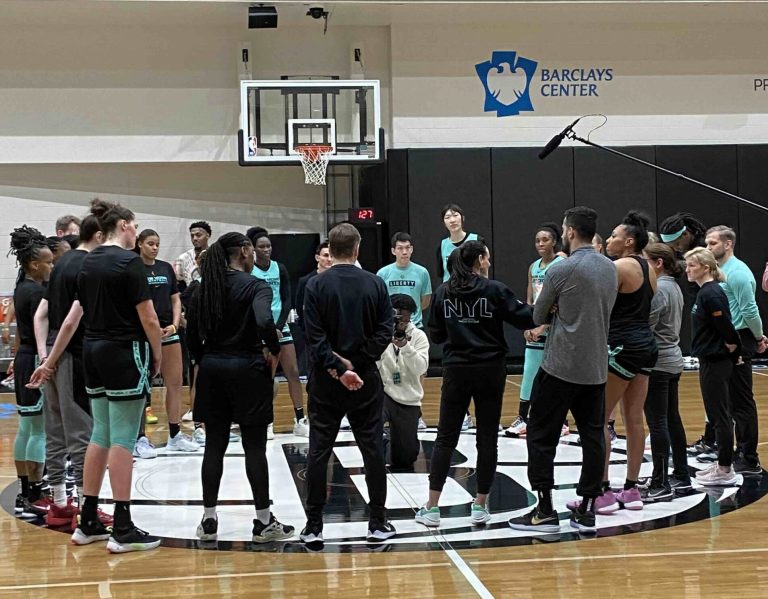 Basketball team huddles on court for discussion.