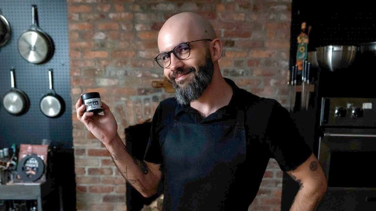 Man holding jar in kitchen with cookware backdrop.