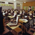 Nun teaching class of girls in uniforms with books.