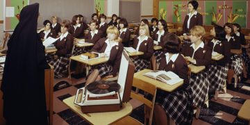 Nun teaching class of girls in uniforms with books.