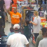 Man raising hand inside a crowded store aisle.