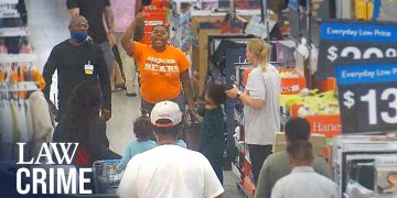 Man raising hand inside a crowded store aisle.