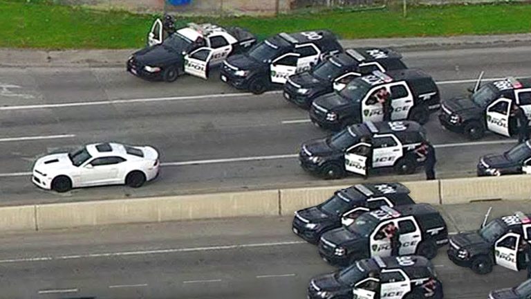 Police cars surround white vehicle on highway