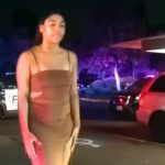 Woman in dress near police cars at night.