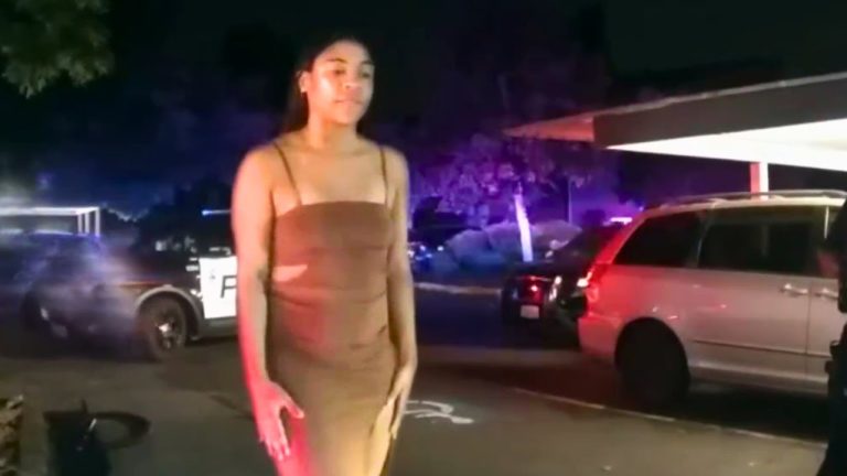 Woman in dress near police cars at night.