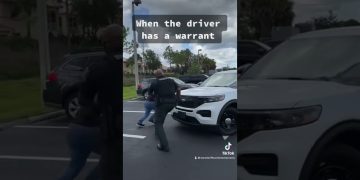 Officer chasing driver near police car in parking lot.