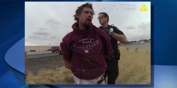 Police officer arresting man in red hoodie.