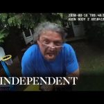 Man confronts police wearing blue shirt, backyard scene.