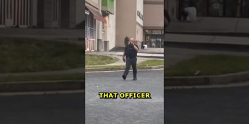 Police officer walking in shopping center parking lot.