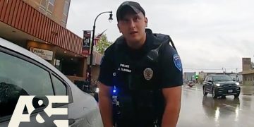 Police officer talking to driver on rainy street.