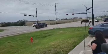 Cars and people at intersection under cloudy skies.