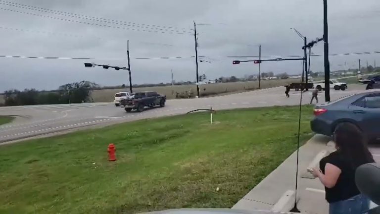 Cars and people at intersection under cloudy skies.