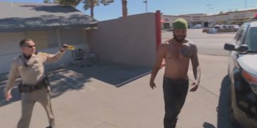 Police officer aiming Taser at shirtless man outdoors