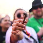 Person holding lit cigar among crowd outdoors.