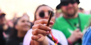 Person holding lit cigar among crowd outdoors.