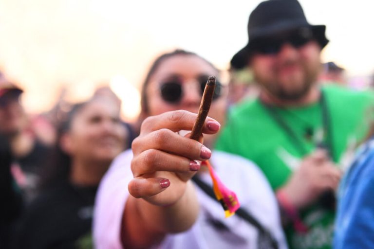 Person holding lit cigar among crowd outdoors.