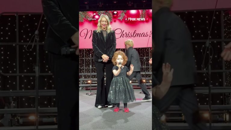 Child singing on stage with woman nearby.