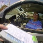 Police officer handing ticket to driver through window.