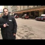 Man reporting on city street with taxis passing.