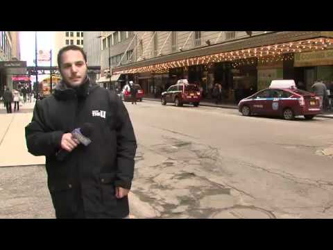 Man reporting on city street with taxis passing.