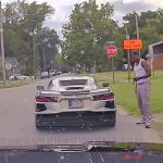 Man standing by sports car near stop sign.