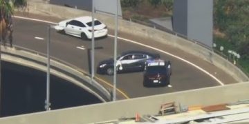 Police cars block dark vehicle on highway ramp.