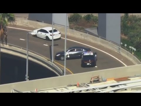 Police cars block dark vehicle on highway ramp.