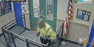 Person entering police station through door with clipboard.