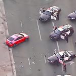 Police cars surrounding red vehicle on road.