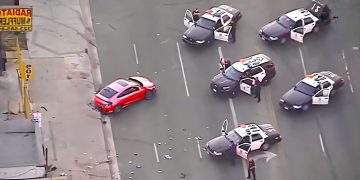 Police cars surrounding red vehicle on road.