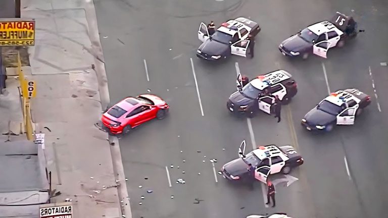 Police cars surrounding red vehicle on road.