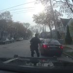 Police officer approaches parked car on residential street.