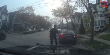 Police officer approaches parked car on residential street.