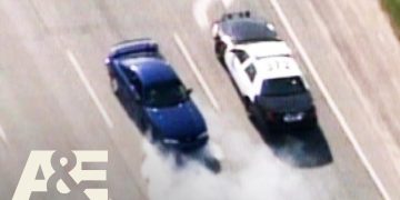 Police car pursuit of a blue vehicle on highway.