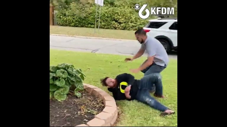 Two people scuffling on grass near road.