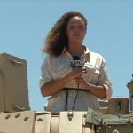 Reporter on military vehicle with microphone.