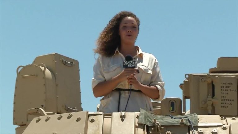 Reporter on military vehicle with microphone.