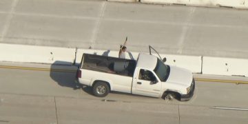 White truck stopped on highway with armed person.