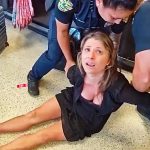 Person detained by airport security officers on floor.