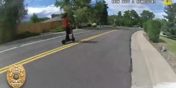 Person riding scooter on suburban street.