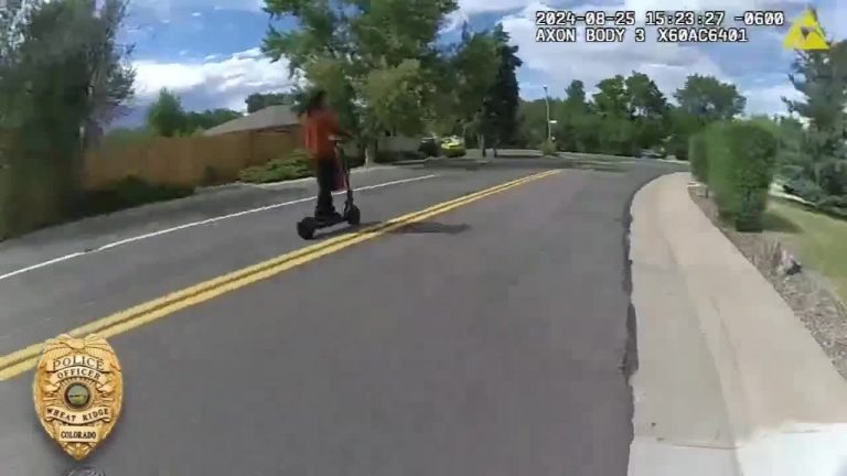 Person riding scooter on suburban street.