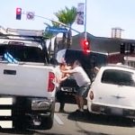 Two people arguing between cars on street.