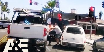 Two people arguing between cars on street.