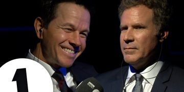 Two men in suits with microphones, smiling.