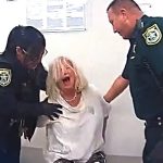 Police officers restrain distressed woman in interrogation room.