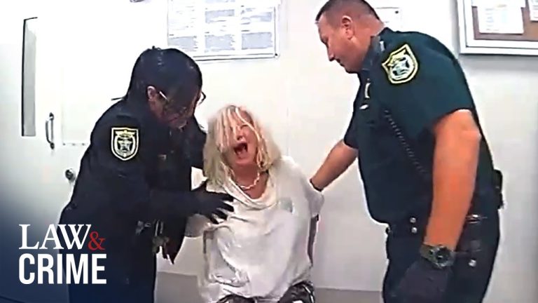 Police officers restrain distressed woman in interrogation room.