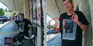 Man outside store holding sandwich in raised hand.