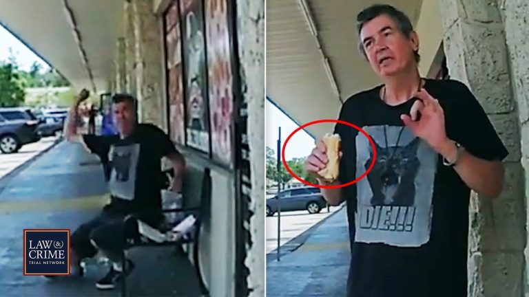 Man outside store holding sandwich in raised hand.